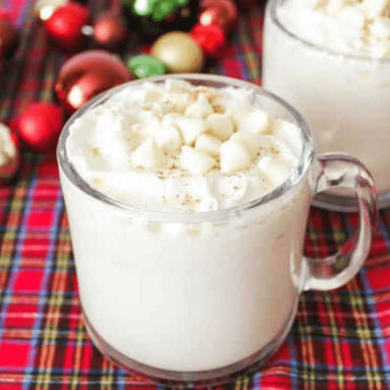 Close up of a whipped cream topped White Hot Chocolate with white chocolate chips on a red plaid tablecloth.