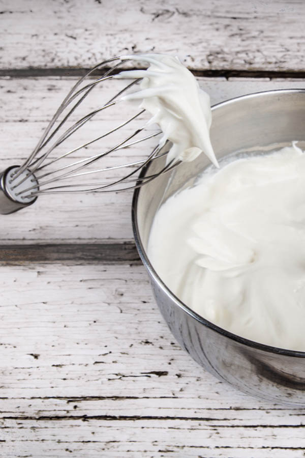 Cool whip to frost an angel food pineapple dump cake in a metal mixing bowl, with a hand mixer whisk attachment.