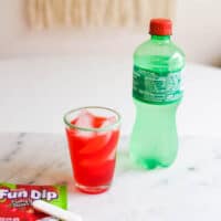 Bright Pink drink in a glass next to a package of Fun Dip and a bottle of Sprite.