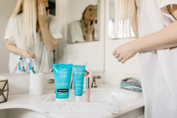 Anti aging skin care products from Neutrogena on a bathroom counter with a woman looking in the mirror.