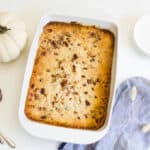 Pumpkin Dump Cake Recipe in a white baking dish next to a fake pumkin and plates.