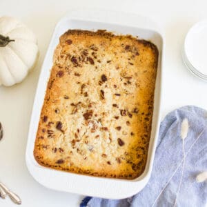 Pumpkin Dump Cake Recipe in a white baking dish next to a fake pumkin and plates.