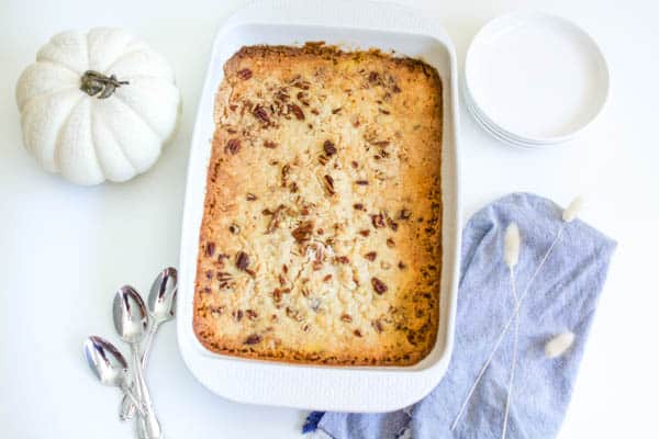 A baking dish with an eggless pumpkin dump cake in it next to a fake pumpkin and some dessert plates. 