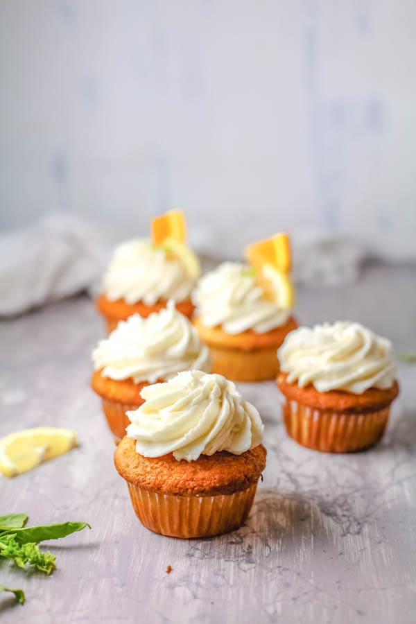 White wine sangria cupcakes on a table decorated with sangria frosting and orange pieces.