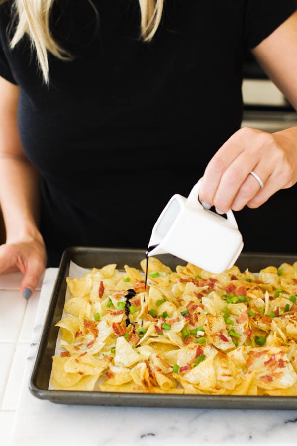 girl drizzling balsamic over blue cheese nachos on a sheet pan