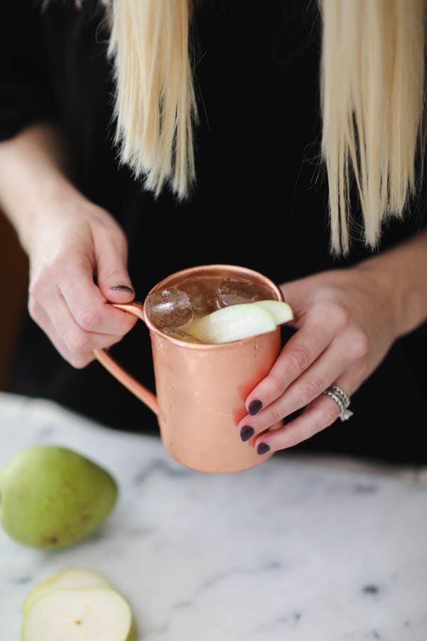 Woman holding a pear mule in a copper mug.