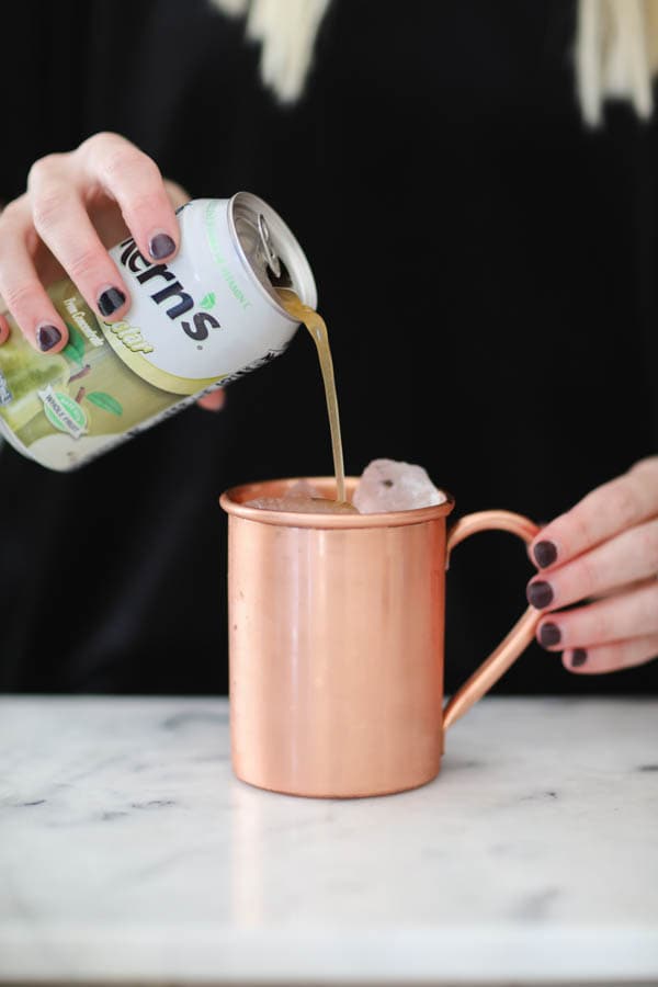 Adding pear nectar to a moscow mule in a copper mug.