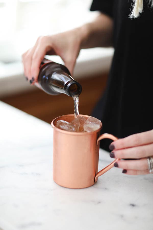 Adding ginger beer to a pear mule recipe in a copper mug. 