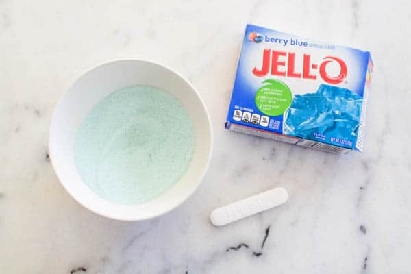 A small bowl of blue Jello powder on a counter next to the Jello box. 