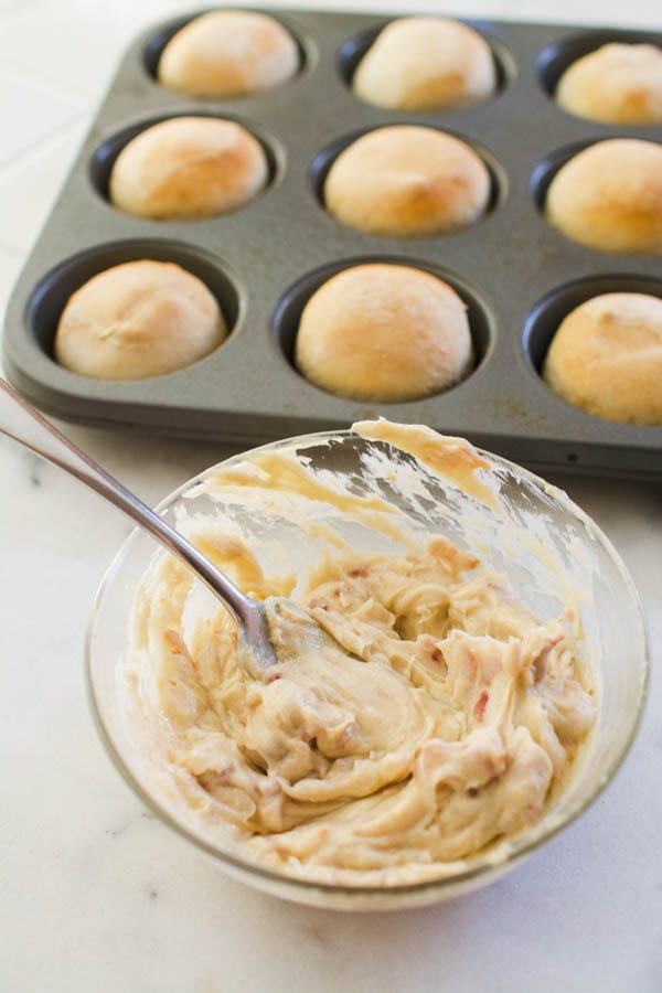 A muffin pan with cooked dinner rolls next to a glass dish holding compound butter with bacon and brown sugar.