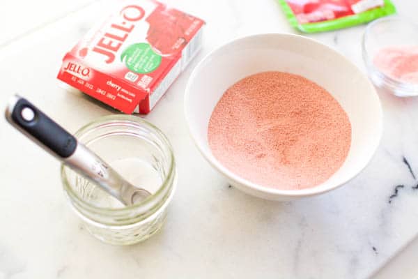 An open box of cherry Jello next to a white bowl with the Jello powder and a small glass bowl with Citric acid. 