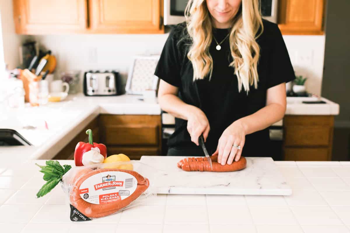 A woman cutting a Kielbasa sausage on a cutting board.