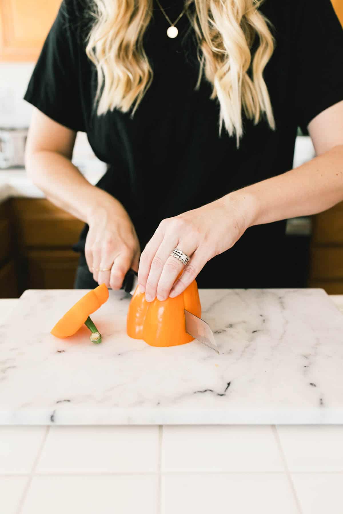A woman cutting an orange bell pepper on a cutting board.