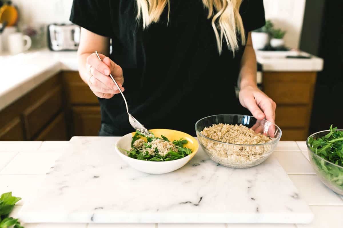 A woman adding quinoa to a bowl with arugula.