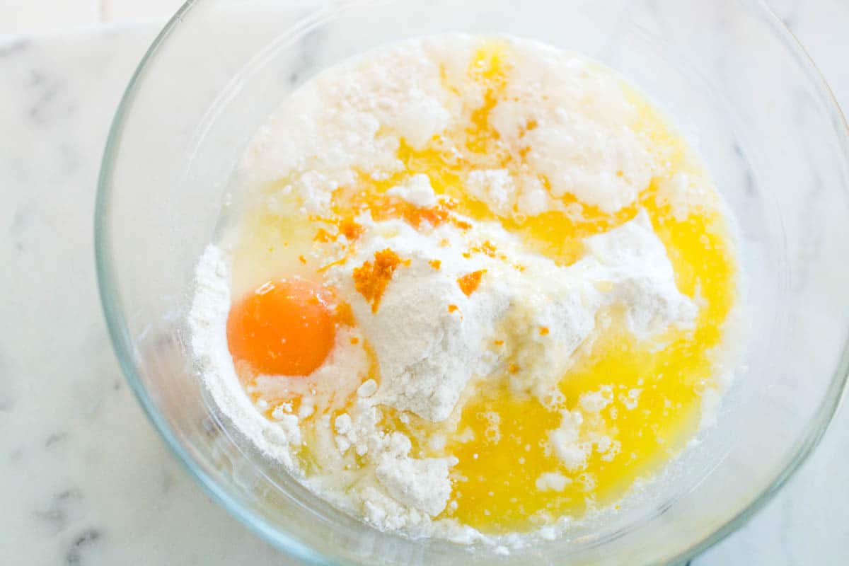 Overhead shot of a mixing bowl with a dry cake mix, an egg, melted butter and orange zest.
