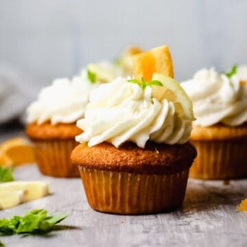 Close up of a frosted cupcake on a table topped with pieces of orange and lime.