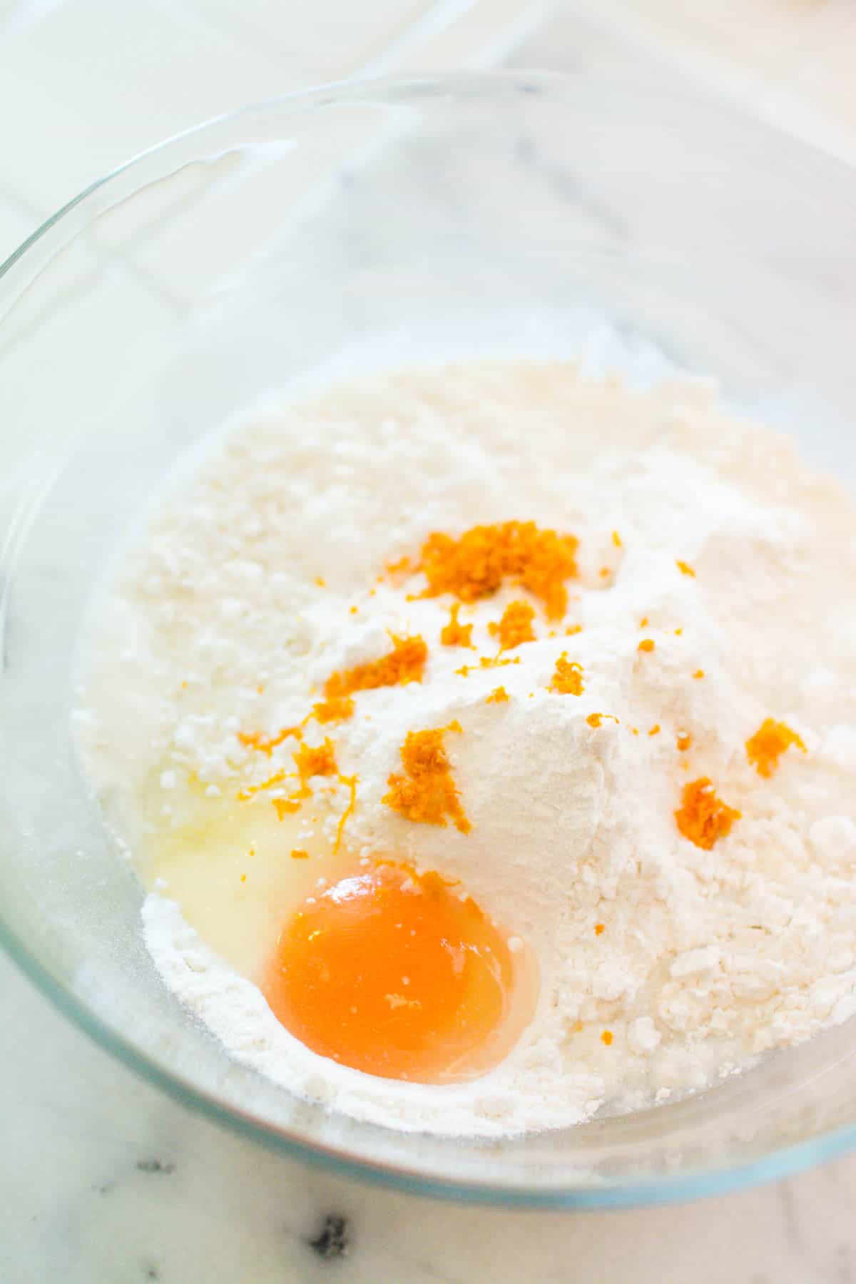 A glass bowl with dry cake mix, an egg and zest of orange in it.