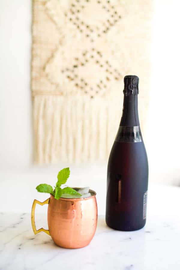 Mimosa Moscow Mule cocktail on a table by a bottle of champagne