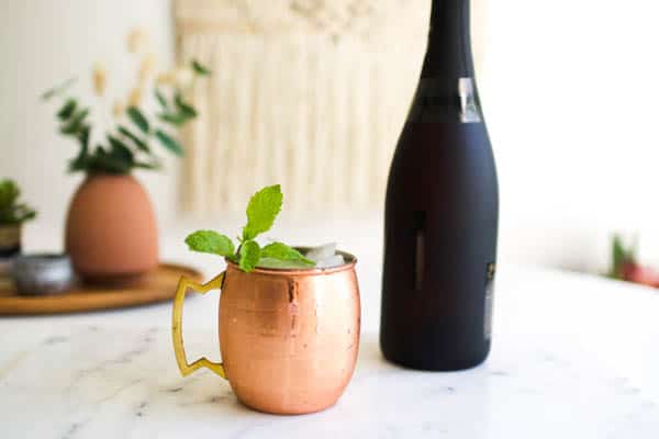a bottle of champagne and a copper moscow mule mug on a table