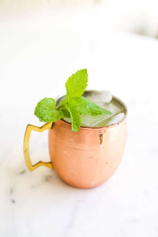 A cocktail in a copper moscow mule mug with mint garnish