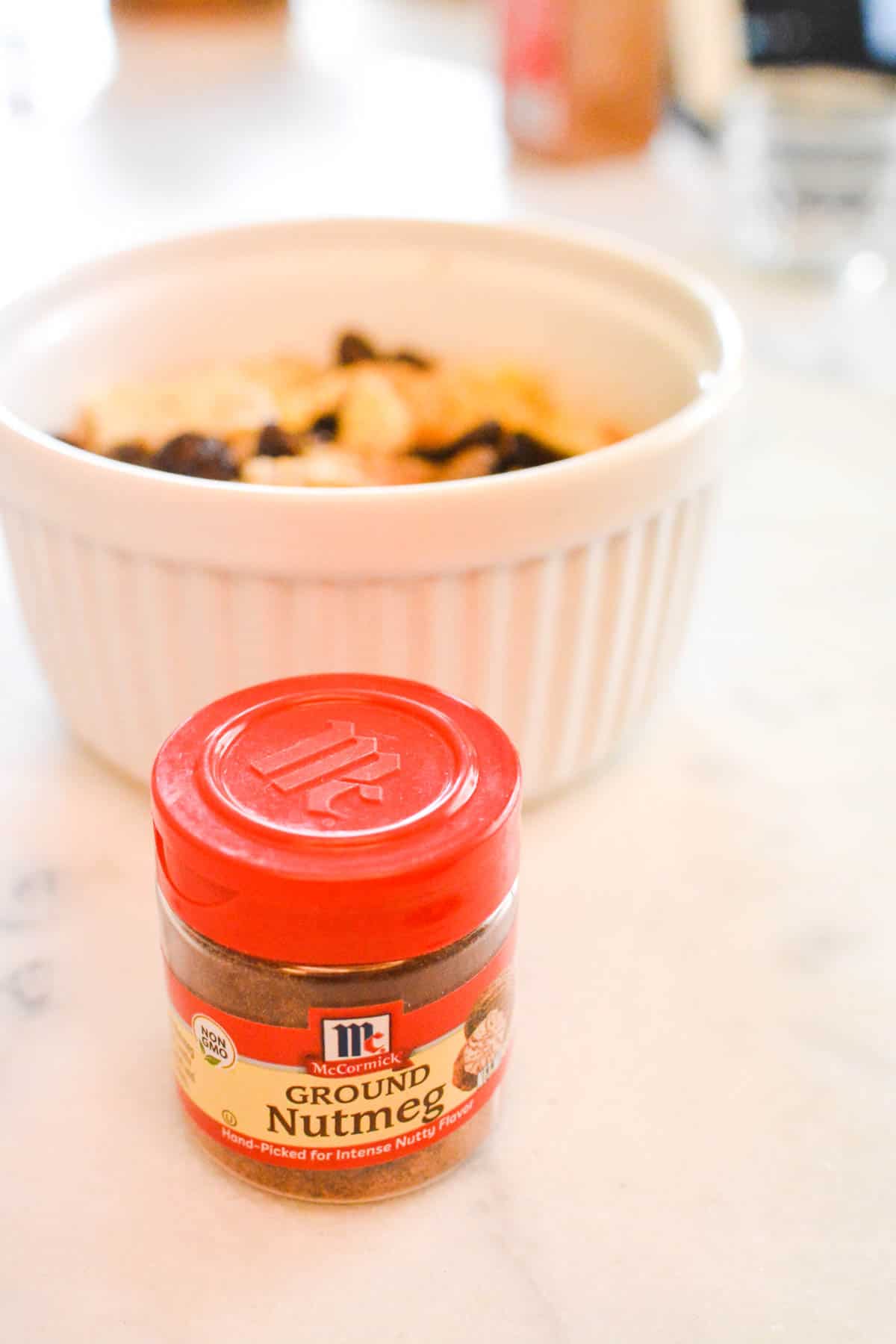 A white ramekin with a small container of nutmeg in front of it.