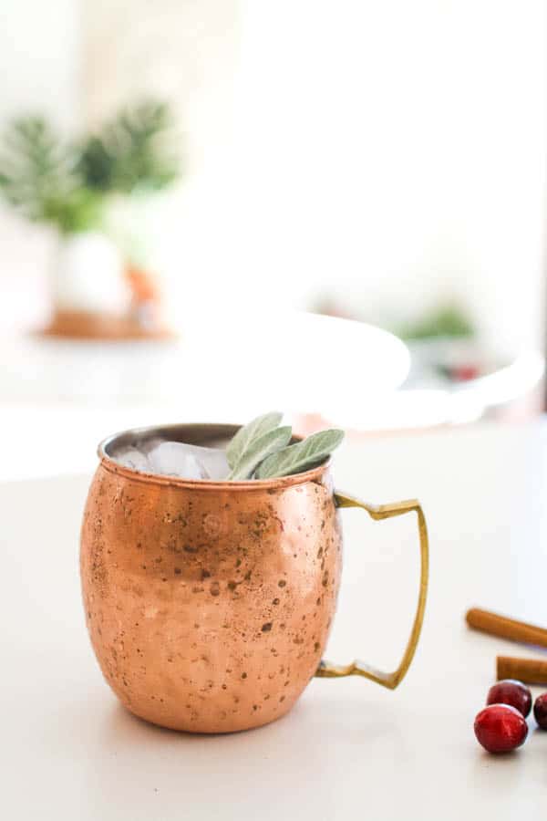 Cranberry Moscow Mule on a table served in a copper mug with a sage garnish.