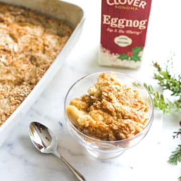 Small glass footed dessert bowl with Eggnog Dump Cake in it next to the baking dish.