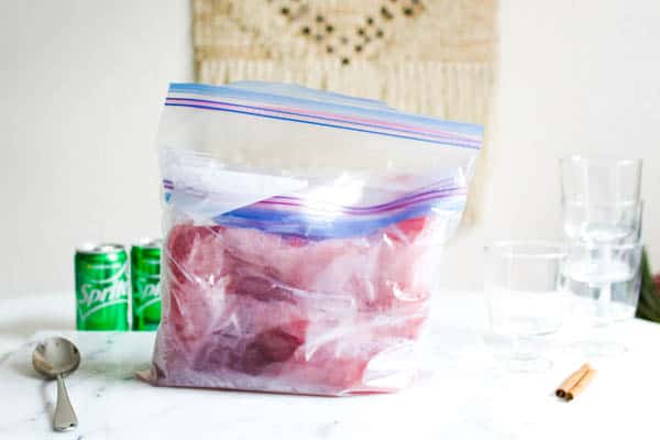 Frozen cranberry vodka slush in a zip bag on table next to lemon lime soda cans. 