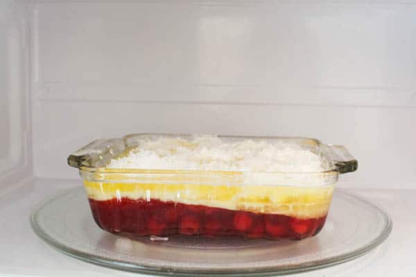 A small glass baking dish holding a cherry pineapple dump cake in the microwave before cooking. 