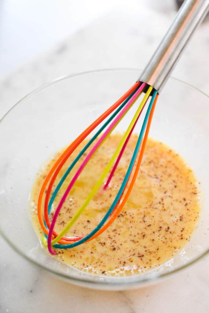 An egg mixture with cinnamon in a bowl with a whisk.