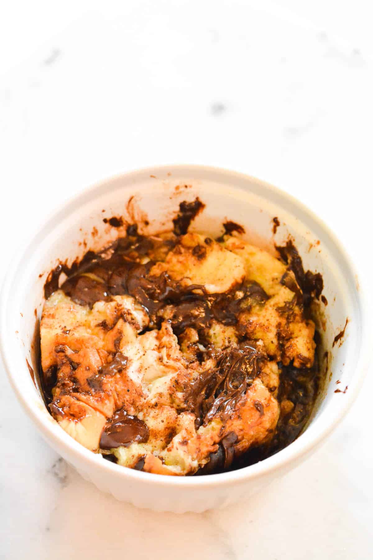A white bowl with chunks of Hawaiian Bread, chocolate chips and an egg mixture after being cooked in the microwave for a minute.