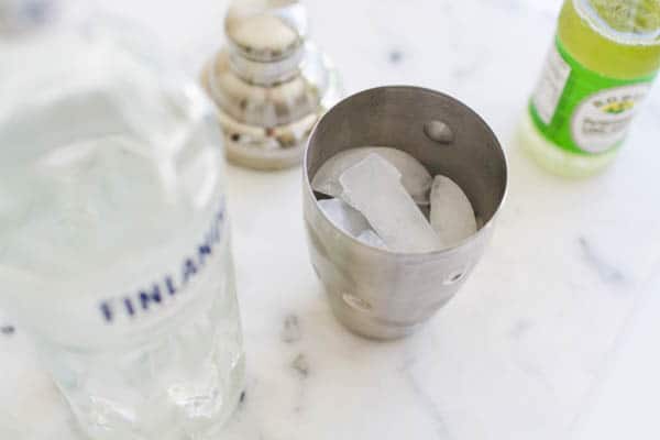 Ice in a cocktail shaker next to a bottle of vodka.