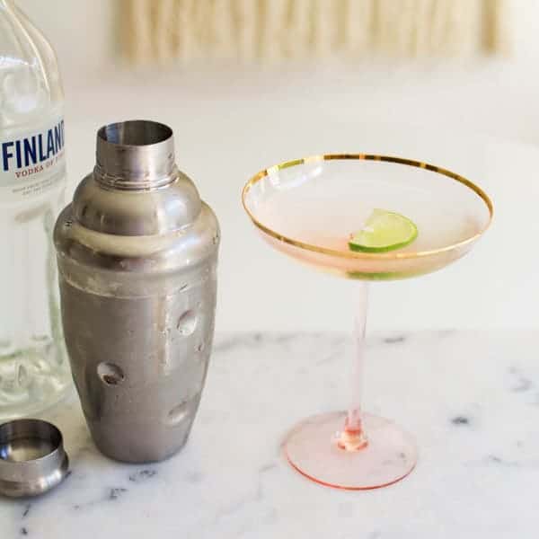 Tall pink and gold coupe glass on a table next to a cocktail shaker.