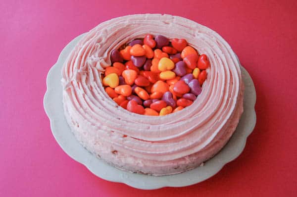 cake on a plate with pink frosting and heart shaped candies in the center as a base to a pinata cake