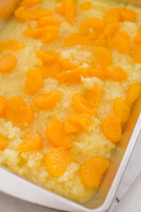 A baking dish with crushed pineapple and mandarin oranges for an easy dump cake.