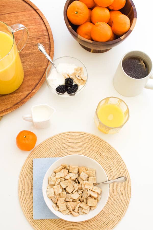 Morning table with cereal, orange juice, tangerines, yogurt and tea.