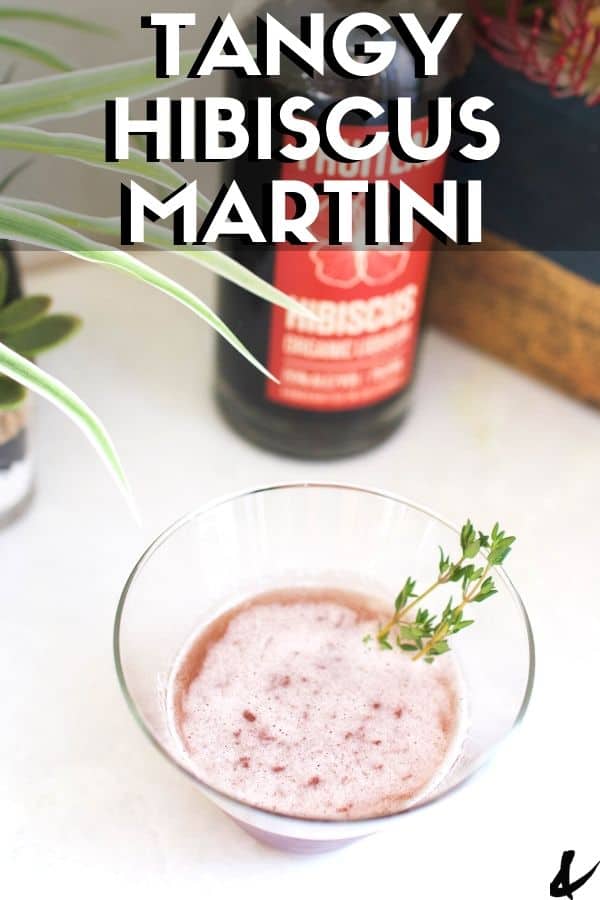 A stemless martini glass with a tangy hibiscus martini in it sitting next to a bottle of hibiscus liqueur.