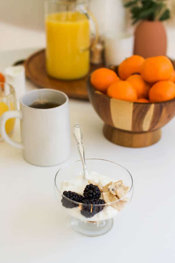 Yogurt in a bowl on a table with a tea cup and bowl of tangerines behind it.