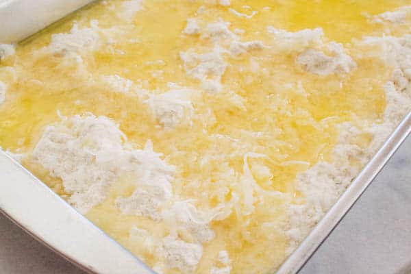 A baking dish with mandarin oranges, crushed pineapple, melted butter, coconut and dry cake mix. 