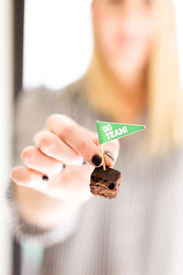 Woman holding a brownie bite on a toothpick with a "go team" flag.