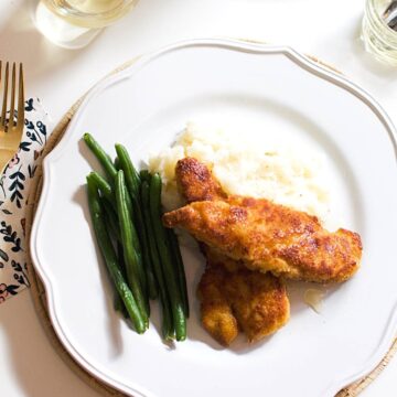 A white dinner plate with Truffle Honey Chicken Tenders, green beans and mashed potatoes.