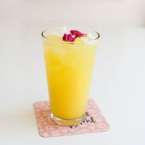 A glass of orange juice and vodka on a table with edible flowers on top.