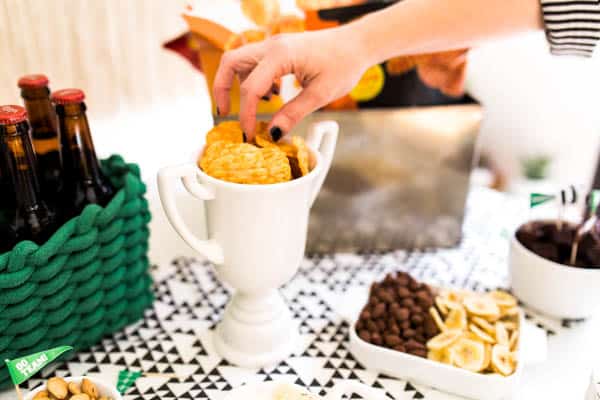 A hand reaching in to take a chip out of a trophy at a football party.