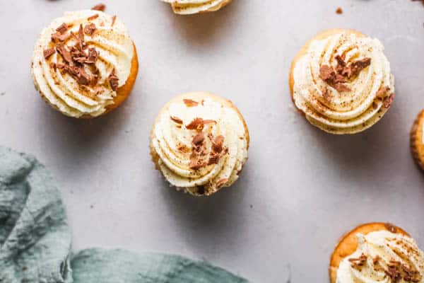 Frosted White Russian Cupcakes on a table with chocolate shavings on top.