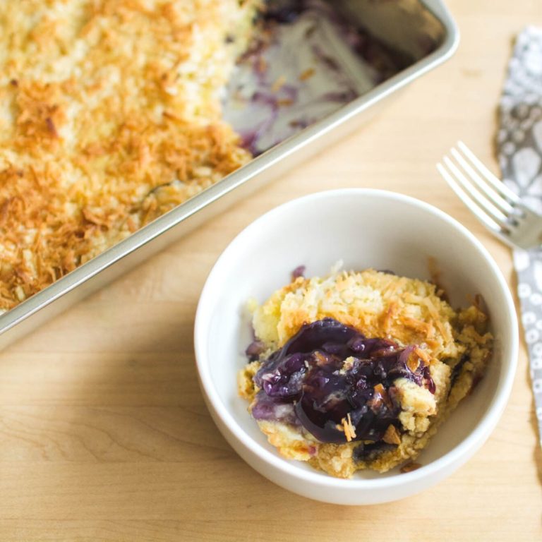 bowl of blueberry pineapple dump cake next to the dessert in the baking pan