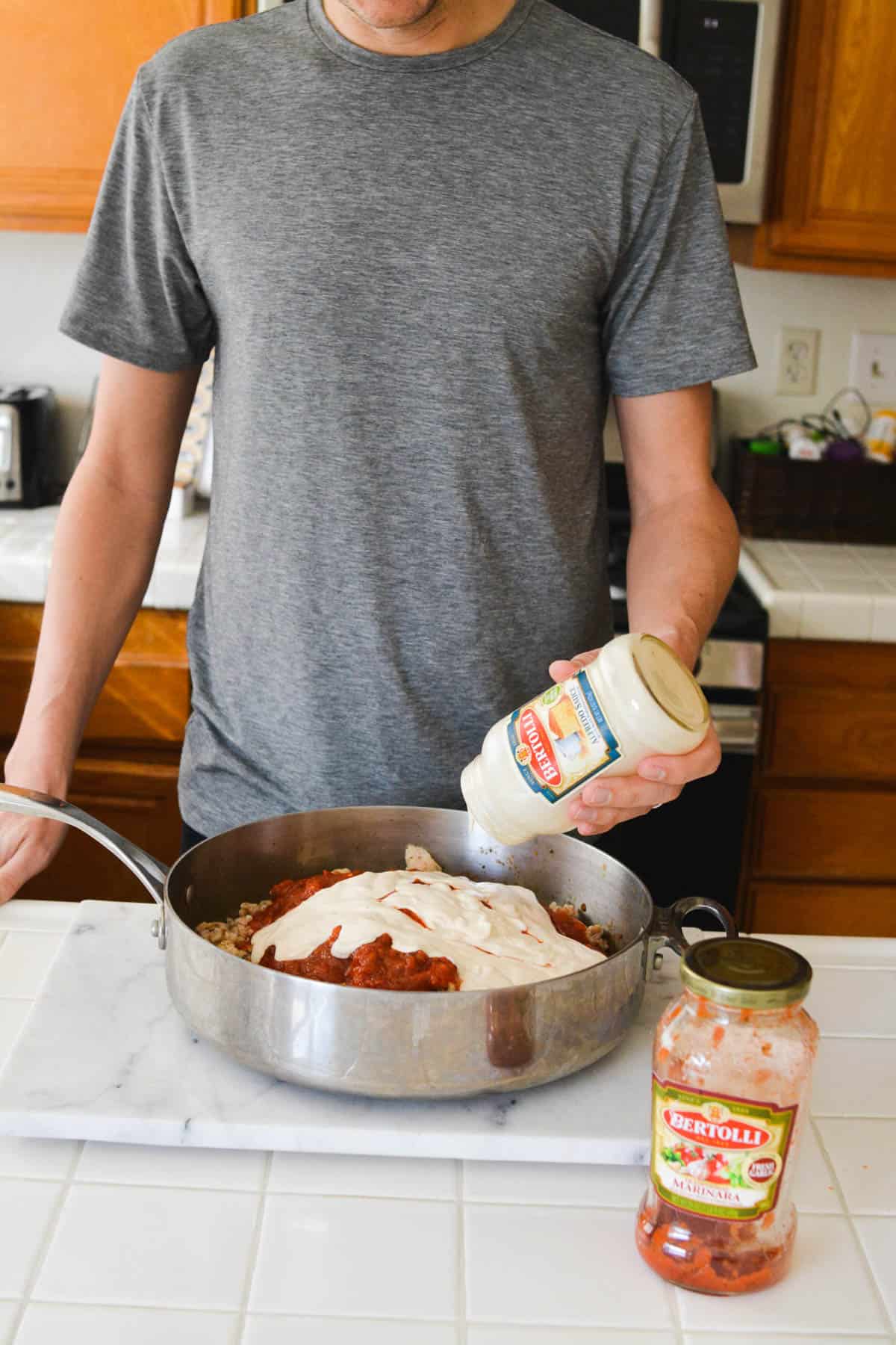 Man adding jarred alfredo sauce to a pan with jarred marinara sauce.