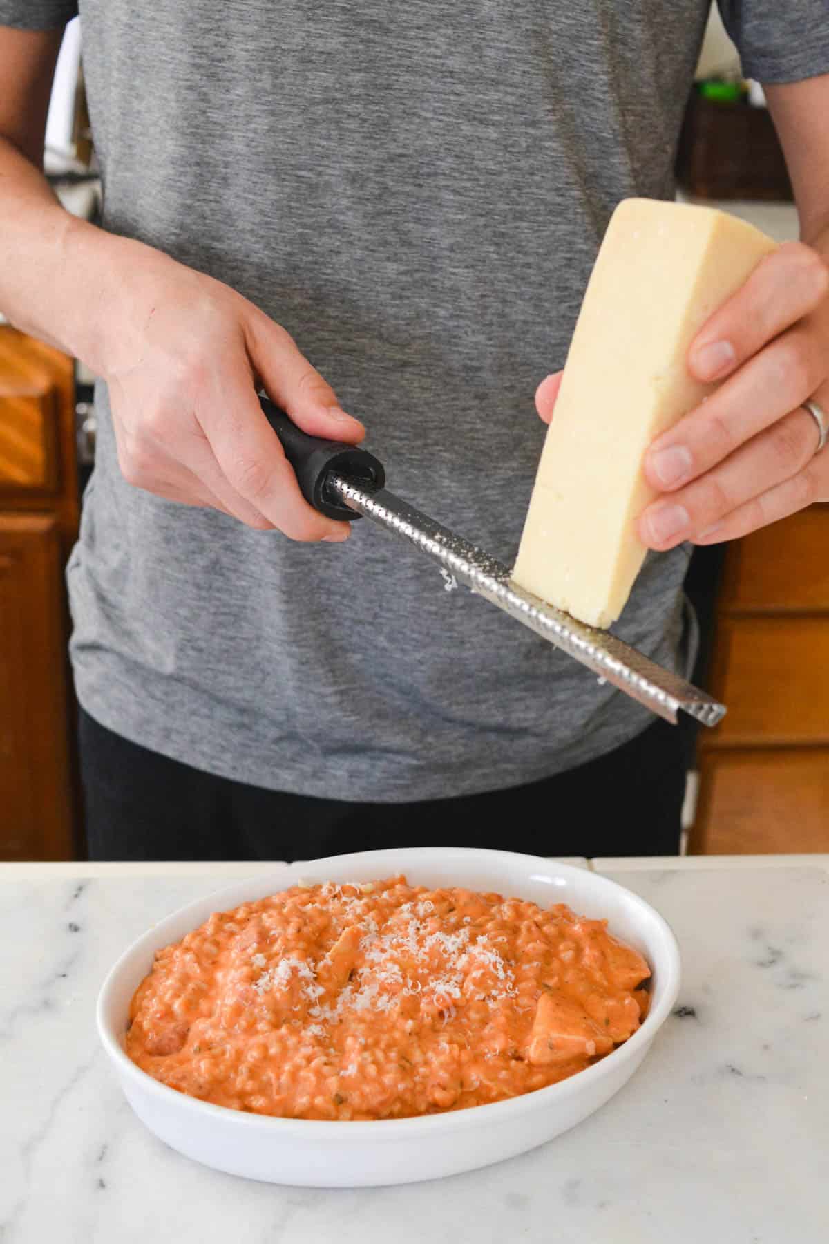Grating parmesan cheese on top of farro topped with sauce.