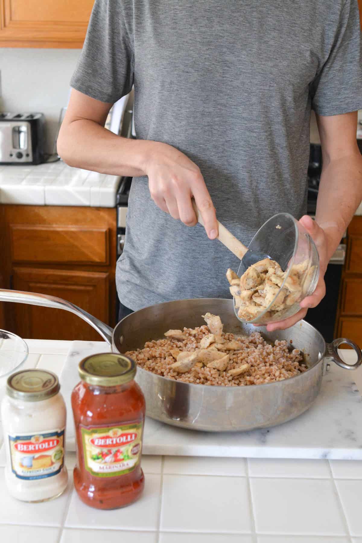 Man adding cooked chicken to a saute pan with farro.