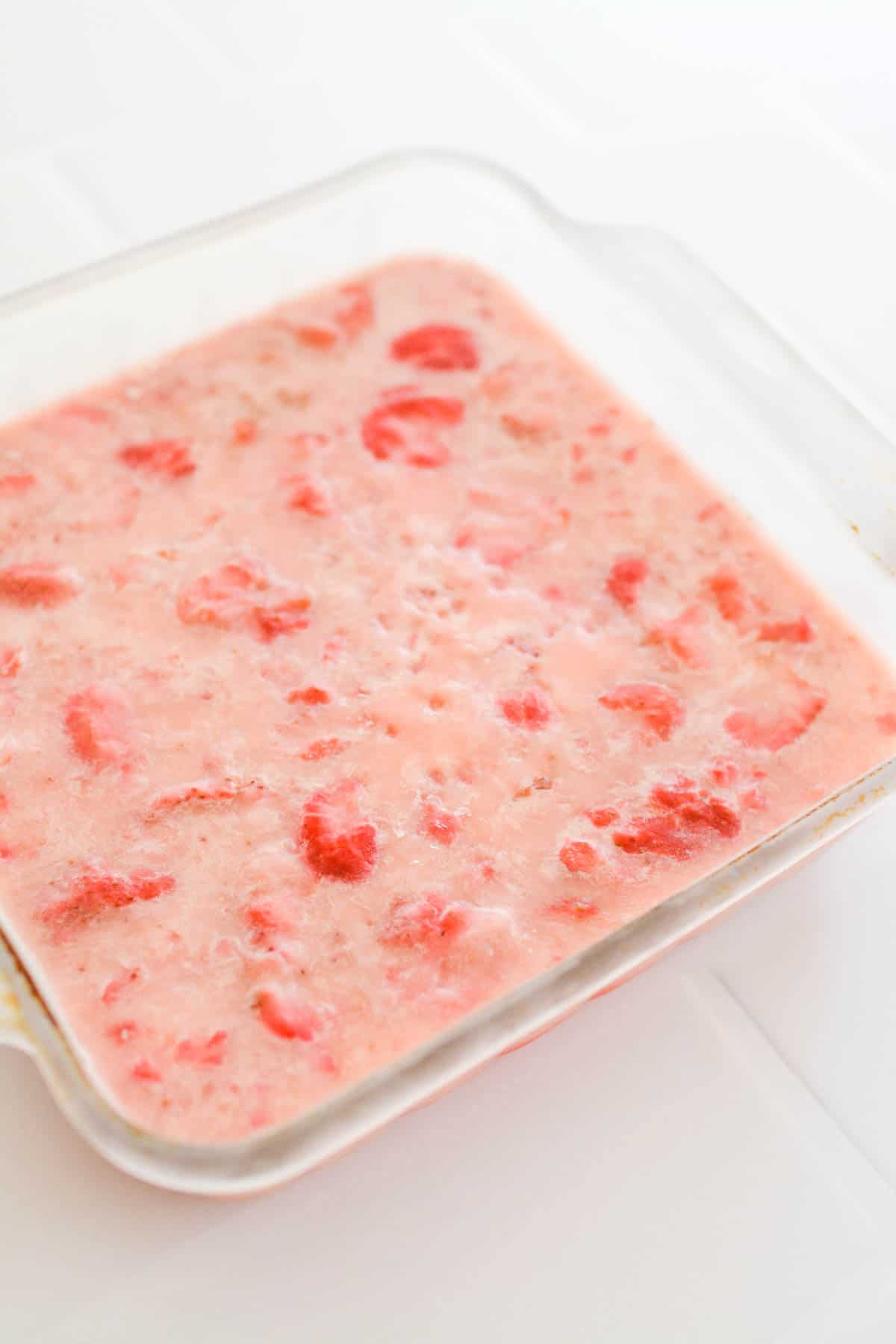 A square glass pan with a frozen strawberry dessert.