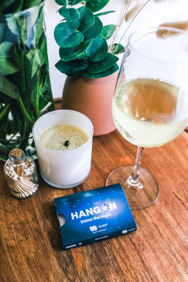 Close up of a glass of wine next to a hangover supplement on a tray.